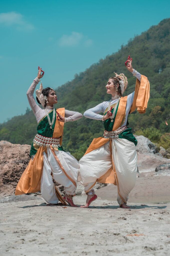 Two women in traditional Odissi dance attire performing on a scenic beach in Puri, India.