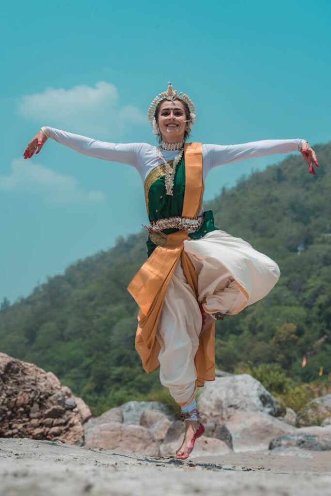 A classical Odissi dancer gracefully poses outdoors with a scenic mountain backdrop, embodying Indian cultural beauty.