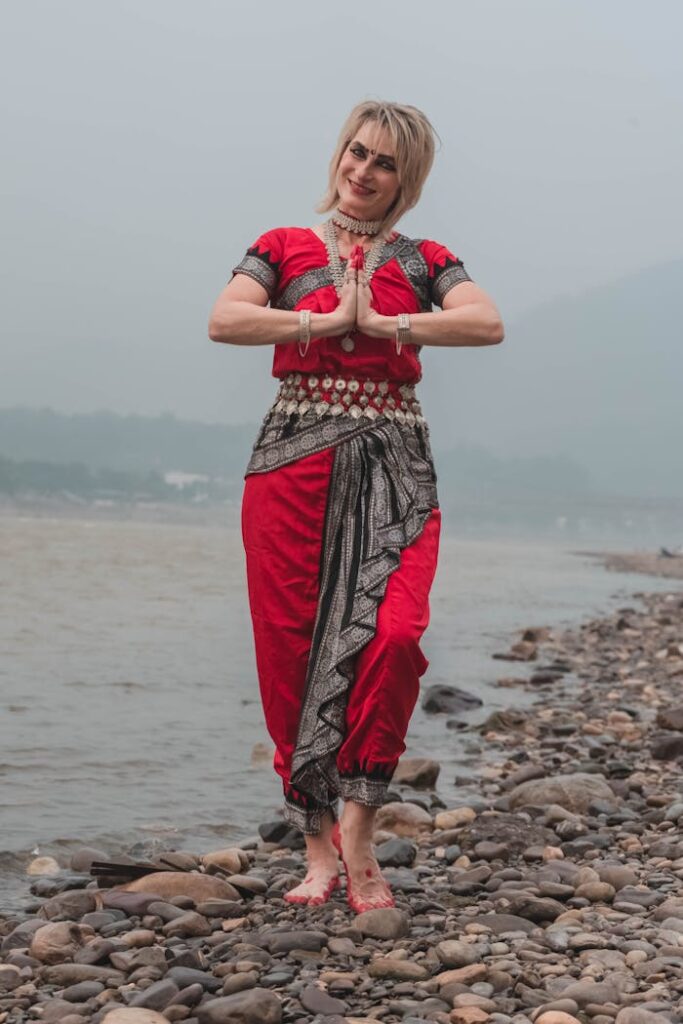 A woman in traditional Odissi dance attire poses gracefully on a rocky riverside, blending culture and nature.