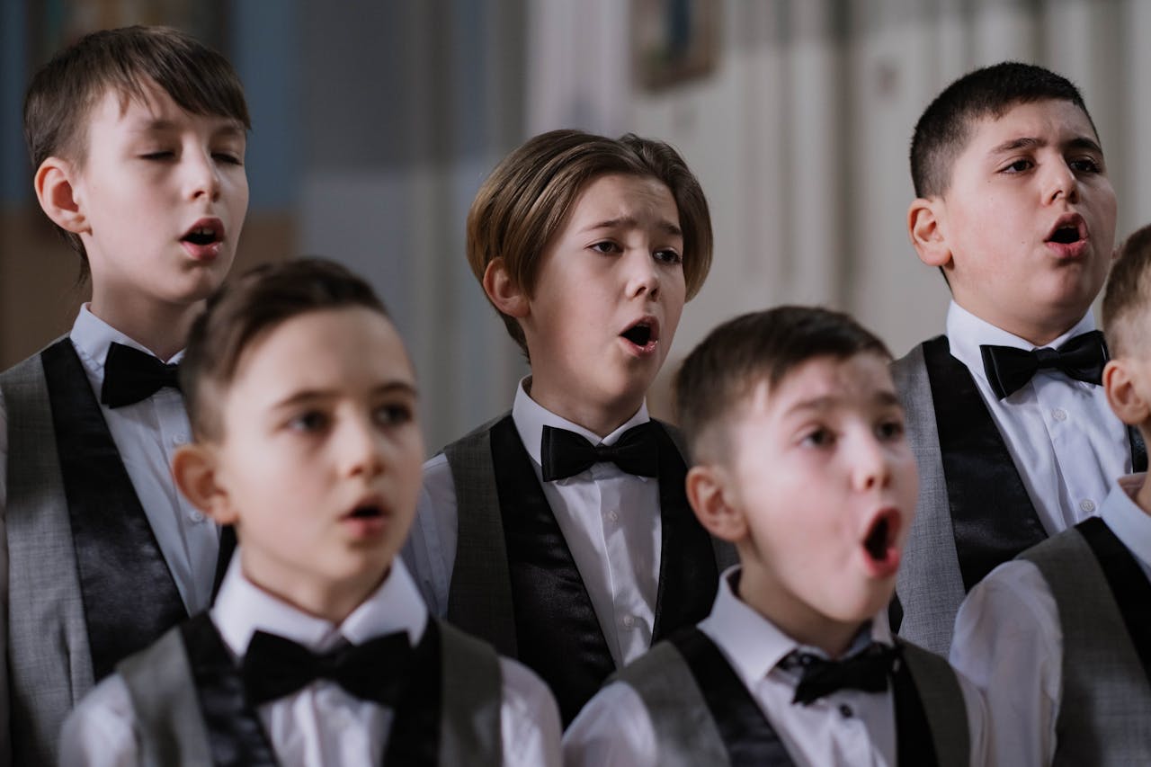 A group of boys performs in a choir, dressed in formal attire, passionately singing indoors.